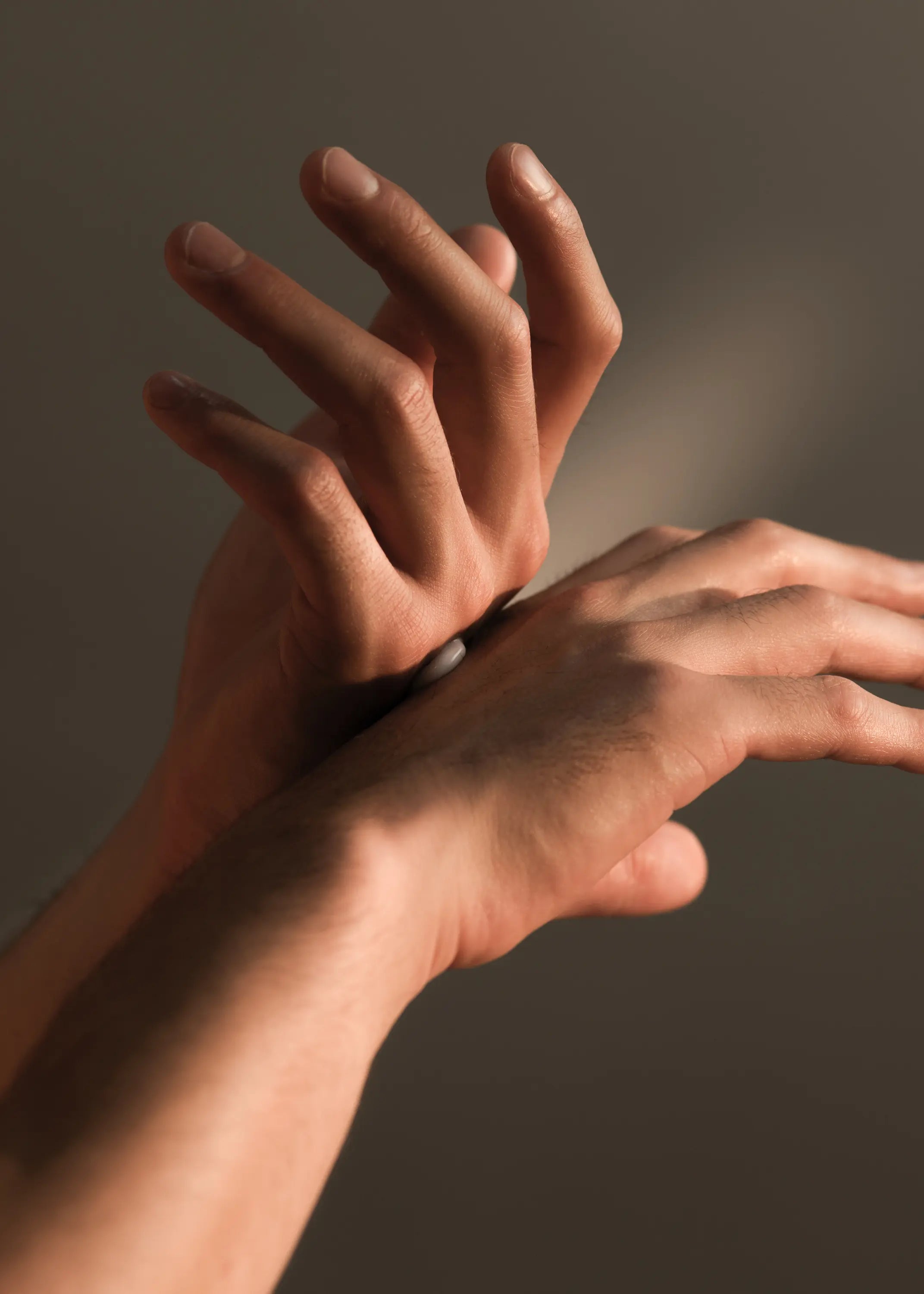 Deux mains s'enduisent mutuellement de crème devant un fond sombre, sous une lumière chaleureuse
