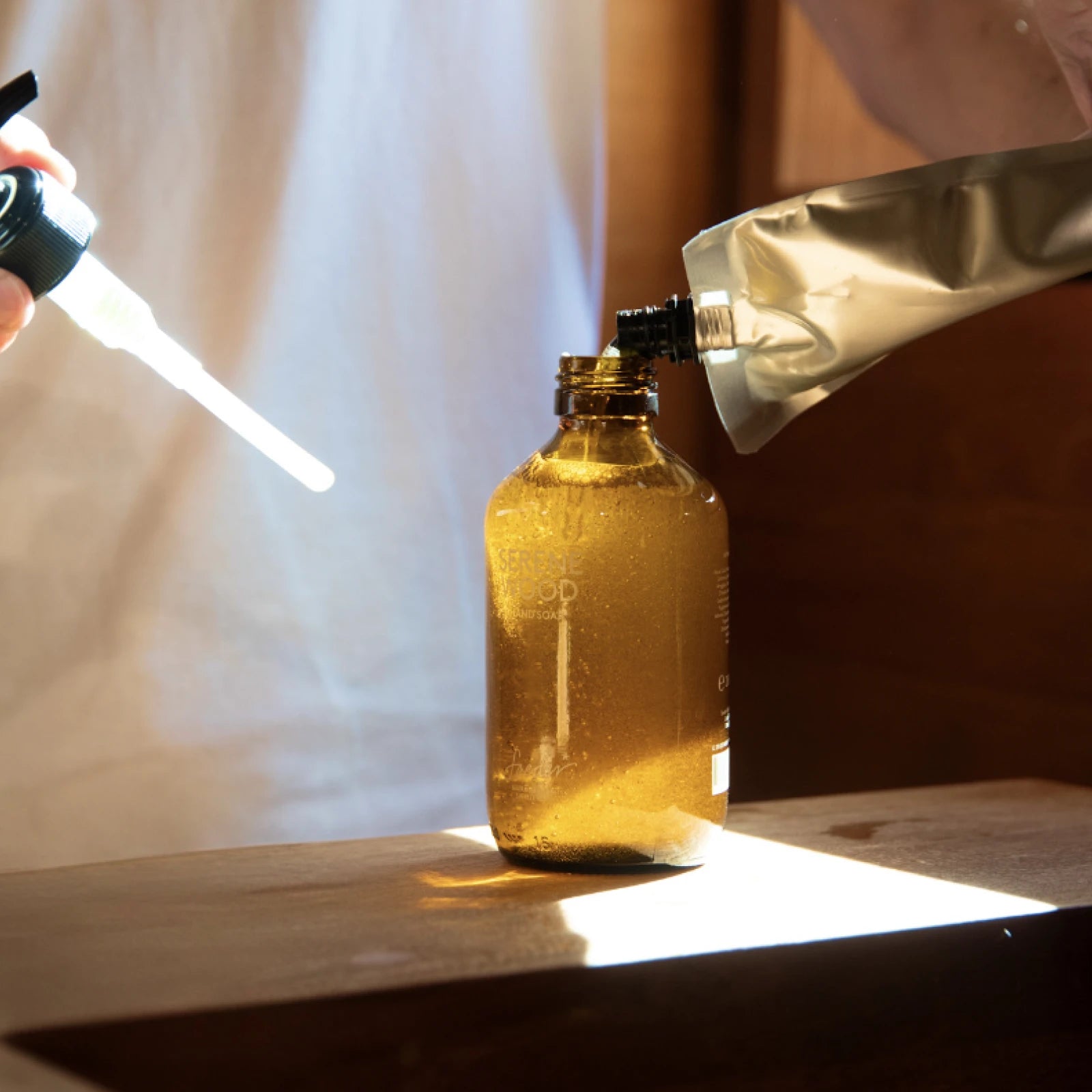 Liquid soap is poured from a refill pouch into a brown glass bottle
