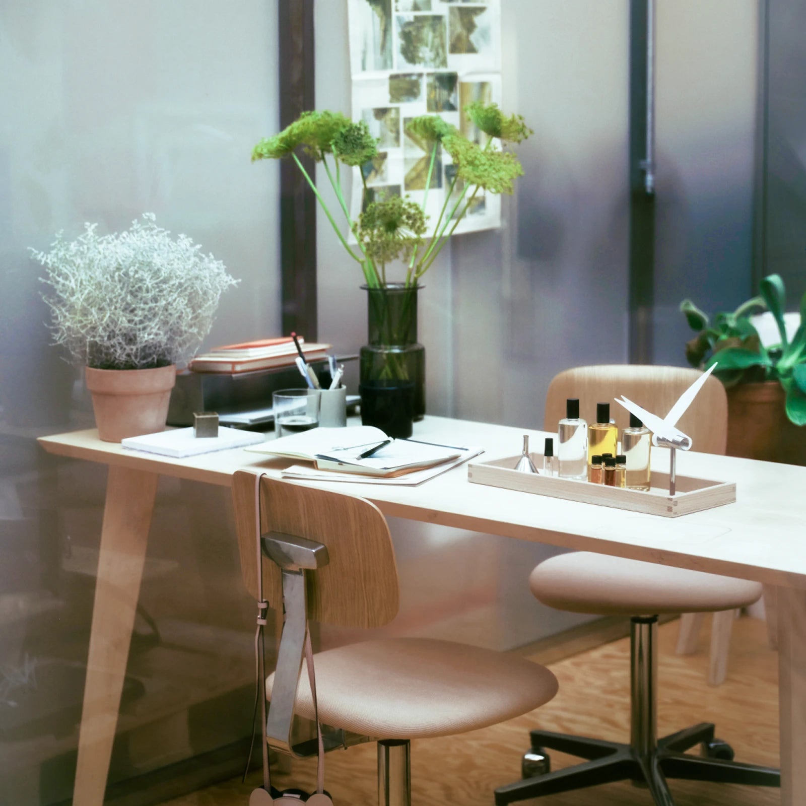 A bright workspace with a wooden table, plants, and small bottles of perfume on a tray