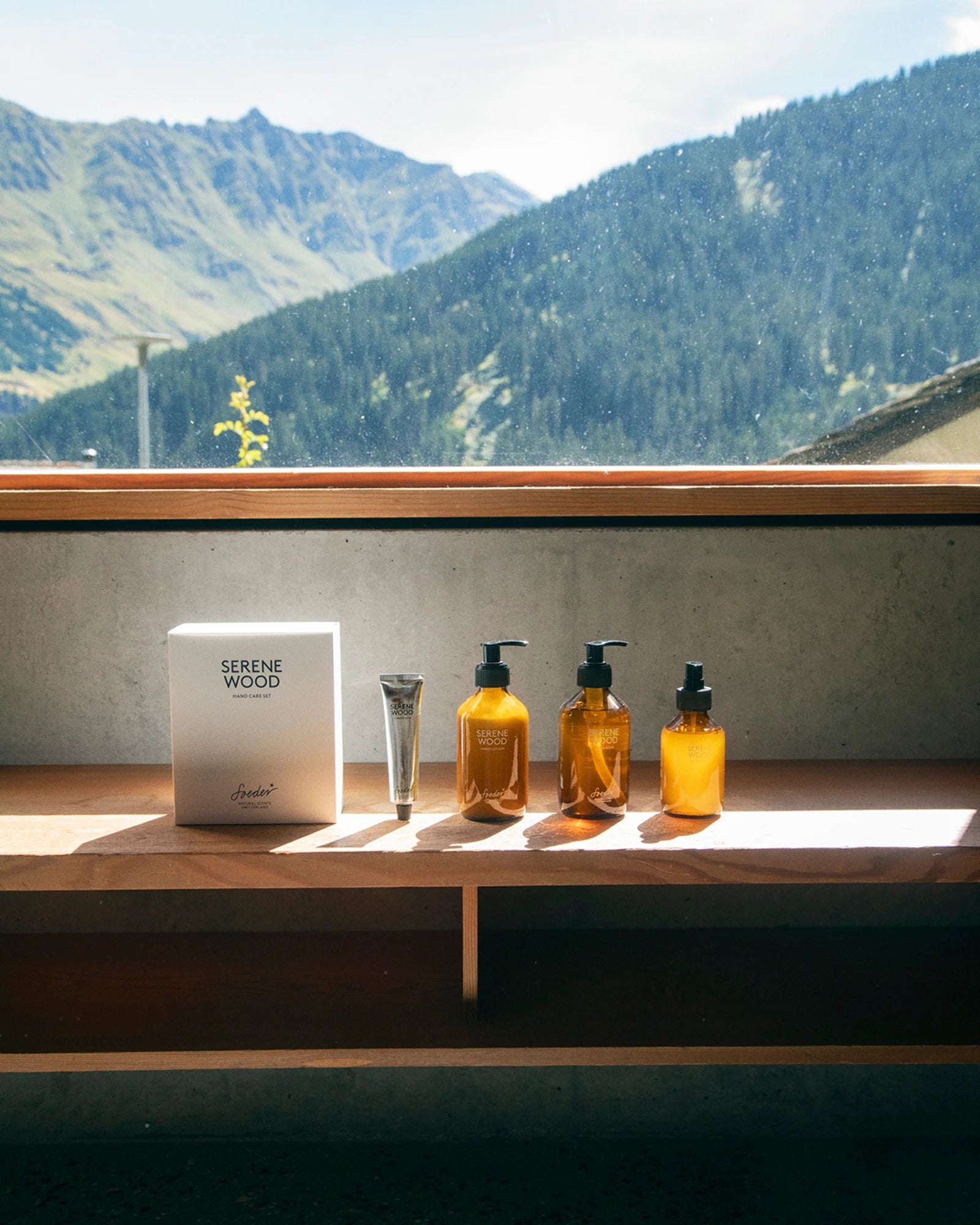 Emballage « Serene Wood », un tube et trois flacons ambrés posés sur un support en bois devant un panorama de montagne
