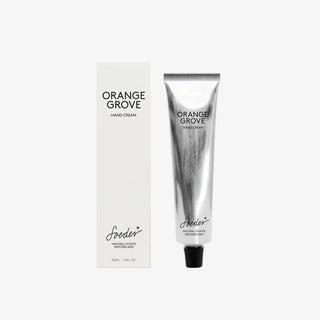 Crème pour les mains Soeder Orange Grove 30 ml dans un tube argenté, à côté d'une boîte pliante blanche sur fond gris clair
